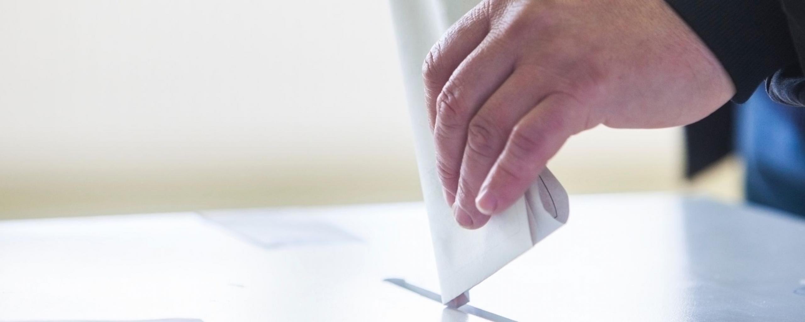 headerafbeelding gemeenteraadsverkiezingen 2022, fot van een hand die een stembiljet deponeert in een bak